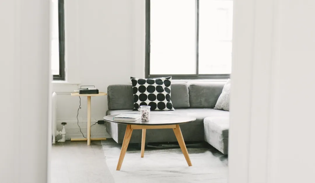 Bright living room with a gray sectional sofa, a black and white polka-dot pillow and a round wooden coffee table under tall windows