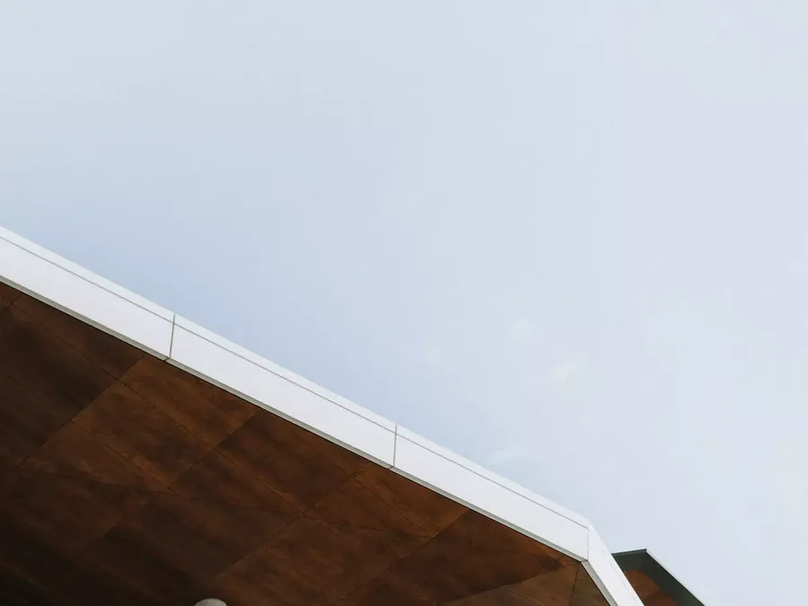 Low-angle photo of a modern roof edge with wood soffit panels against a pale sky