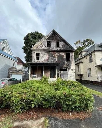 Fire-damaged two-story house with charred siding and boarded windows, the kind of house a cash buyer purchases as-is