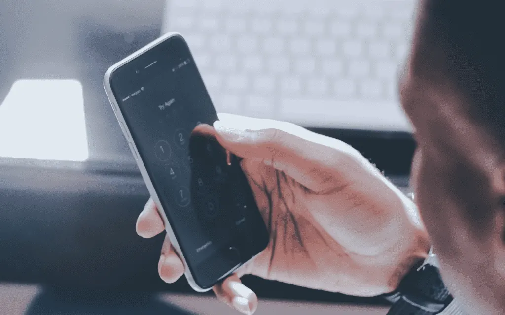 Close-up of a hand holding a smartphone in front of a laptop keyboard