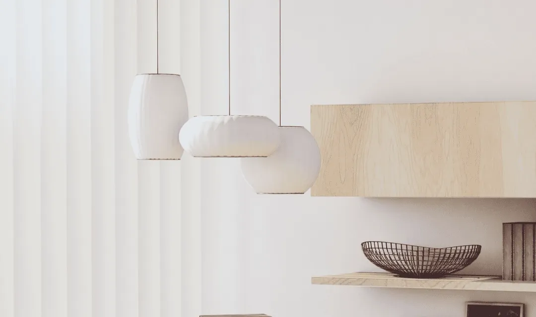 Bright, uncluttered room corner with three white paper pendant lamps hanging over a light wood floating shelf with a wire bowl and books