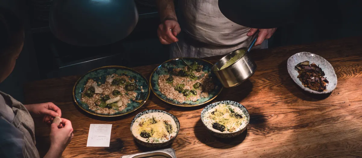 Overhead view of several hands reaching for shared plates of food on a dark wooden table