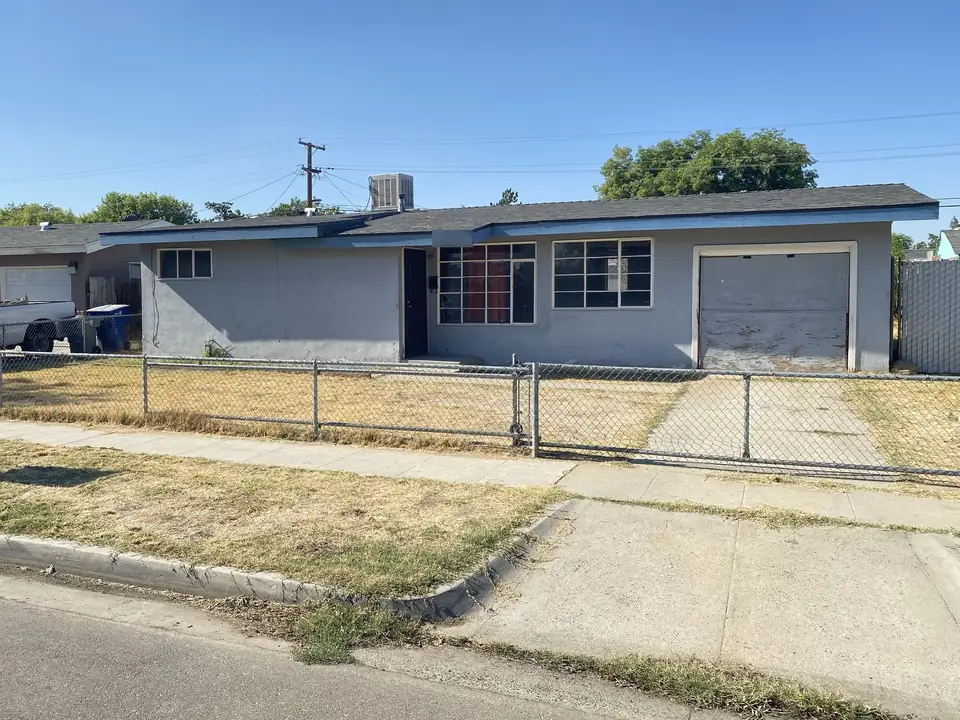Dated ranch house with a dry yard and worn garage door, from a Cash For Houses Fresno transaction